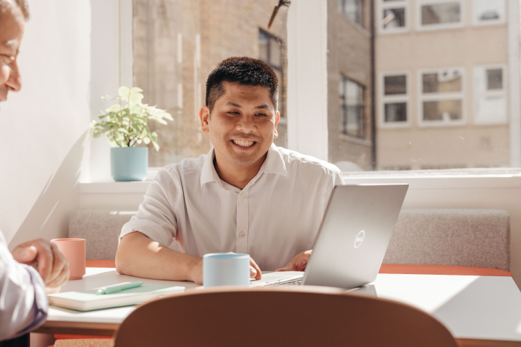 A professional photograph of William Phung, Lendhub’s Portfolio & Credit Manager, a smiling man with short black hair, wearing a white collared shirt looking at something on his laptop while a colleague watches from the side.