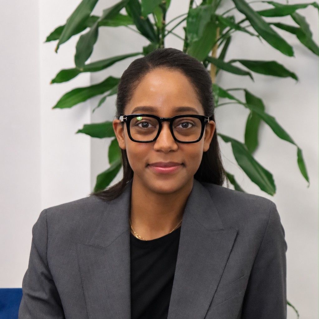 Professional portrait of Theresa Bailey, Lendhub’s Senior Strategic Partnerships Manager, wearing a grey blazer and black glasses, seated in front of a leafy green plant.